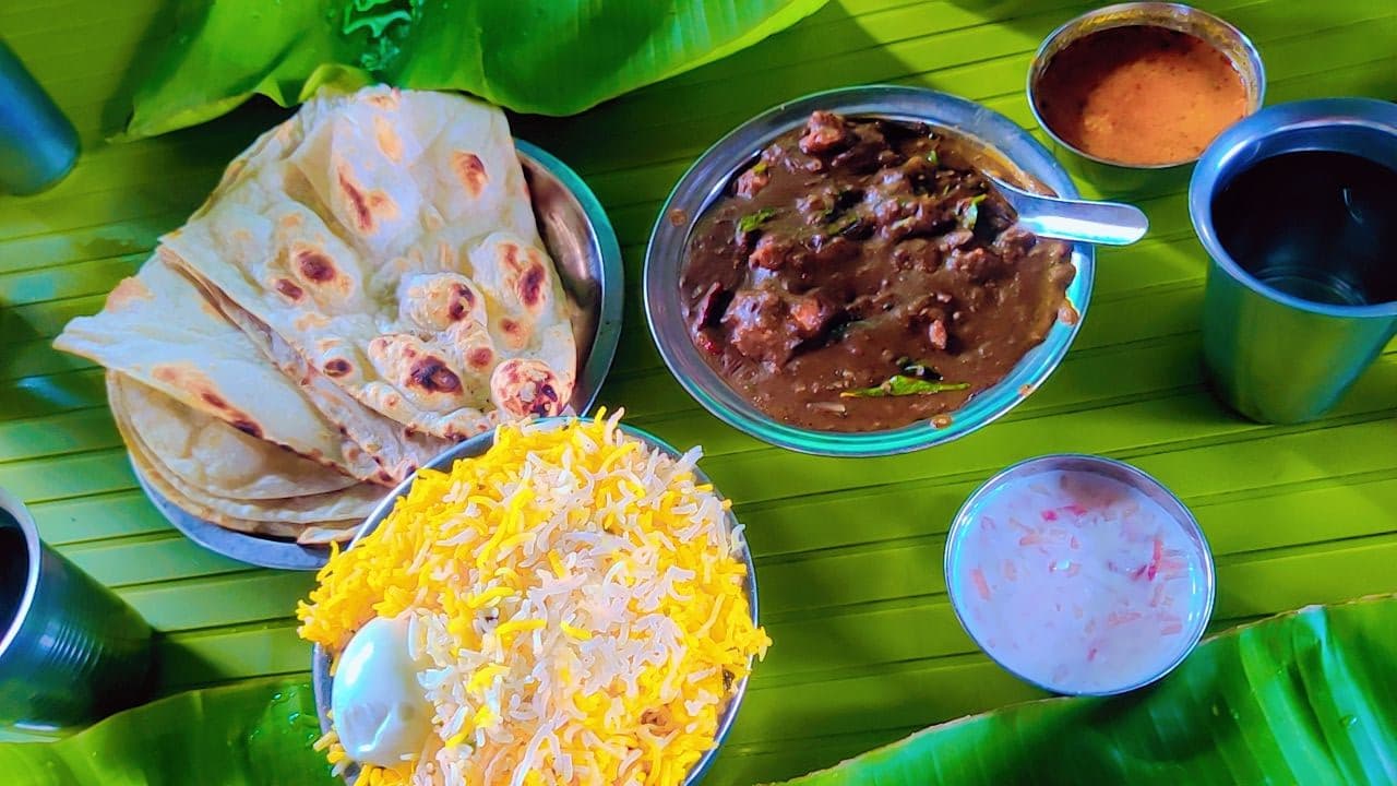 A Hyderabad meal laid out on a banana leaf: biryani, roti, a dark curry and raita.