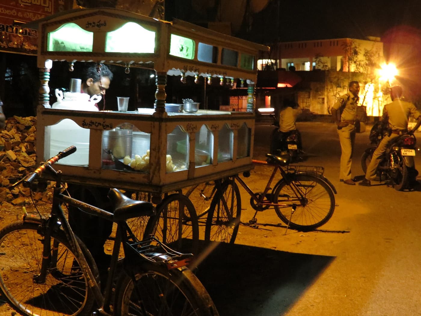 A Hyderabad street food stall at night, lit by a single bulb, with customers waiting at the counter.